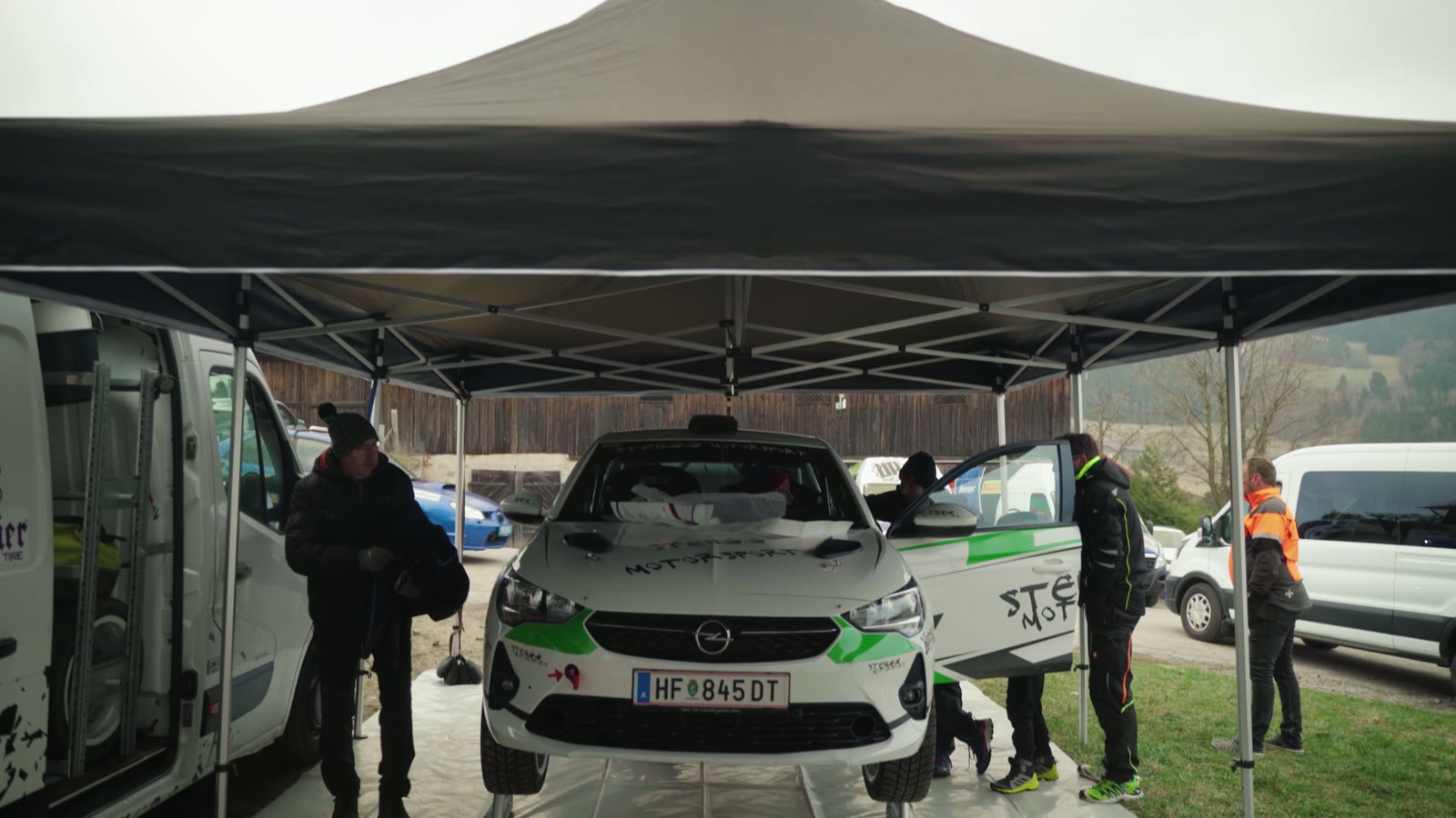 Rallyewagen unter dem Zeltdach im Service, Team und Transporter daneben